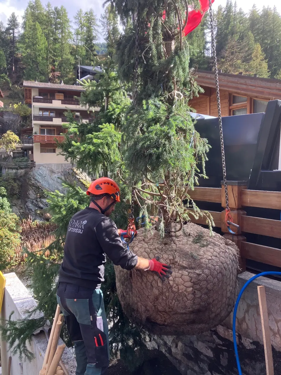 Arbeiter positioniert grossen Naturstein mit Sicherheitsausrüstung per Kletterseil.